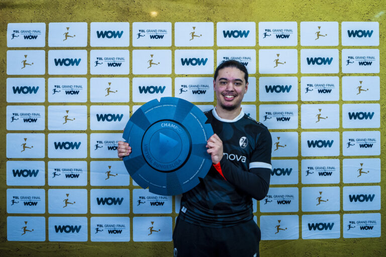 Athlete in uniform smiles while holding a large blue circular trophy in front of a WOW Grand Final backdrop.