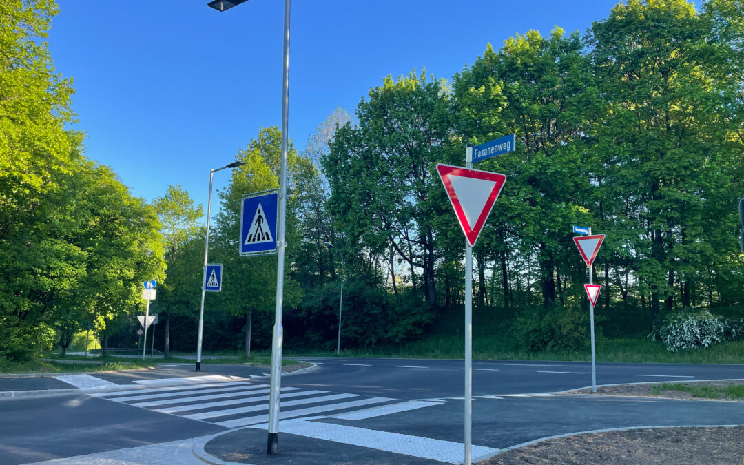 Sunny intersection with yield sign and pedestrian crossing signs beside a tree-lined street labeled Fasanenweg in bright daylight.