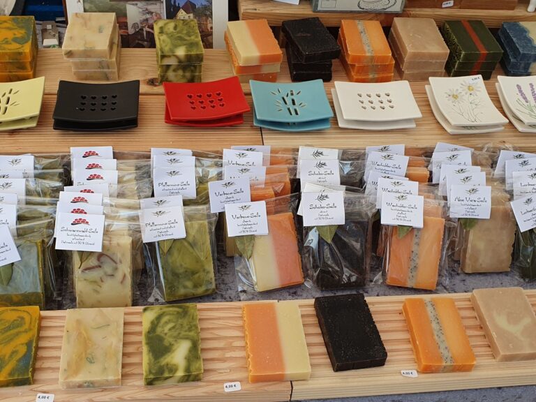 Assorted colorful handmade soaps stacked on a wooden rack with price tags showing 4,00 € in front.