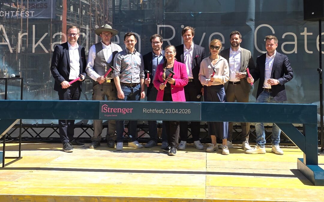 Group of professionals posing on a stage holding hammers at Richtfest, banner reads Richtfest 23.04.2026 in the background.