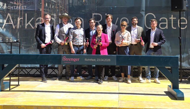 Group of professionals posing on a stage holding hammers at Richtfest, banner reads Richtfest 23.04.2026 in the background.