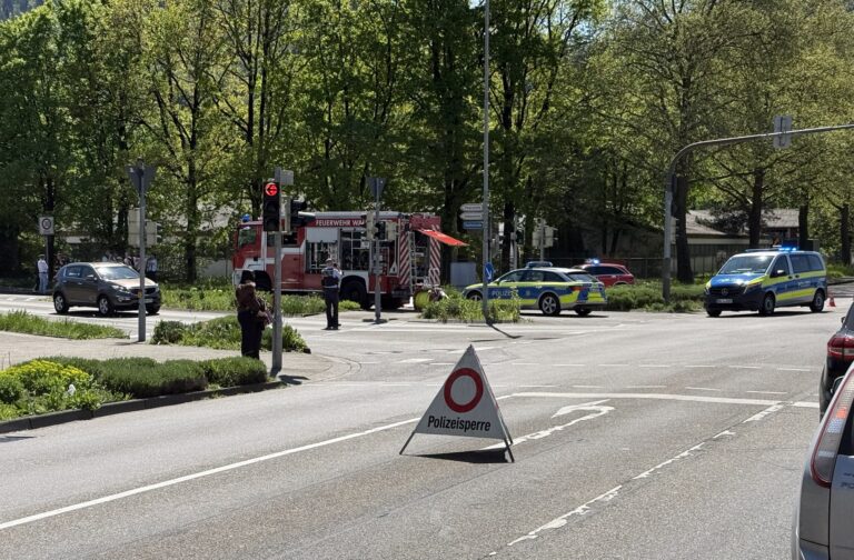Emergency scene at an intersection with a red fire truck, police cars, and officers guarding a blocked street.