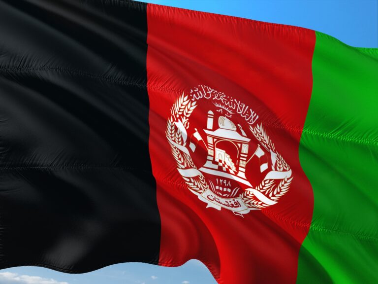Afghan national flag waving in the wind with black, red, and green vertical stripes and emblem at center.
