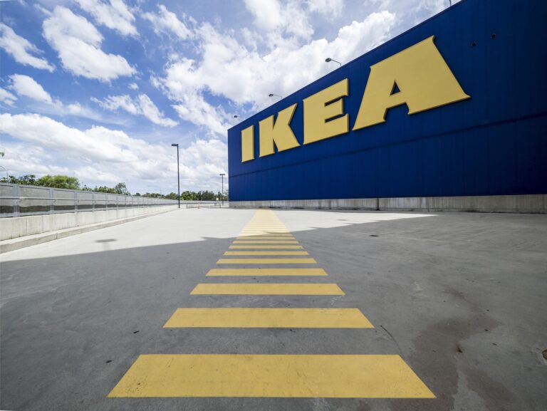Blue IKEA warehouse exterior with a large yellow IKEA logo and yellow ground markings in the foreground.