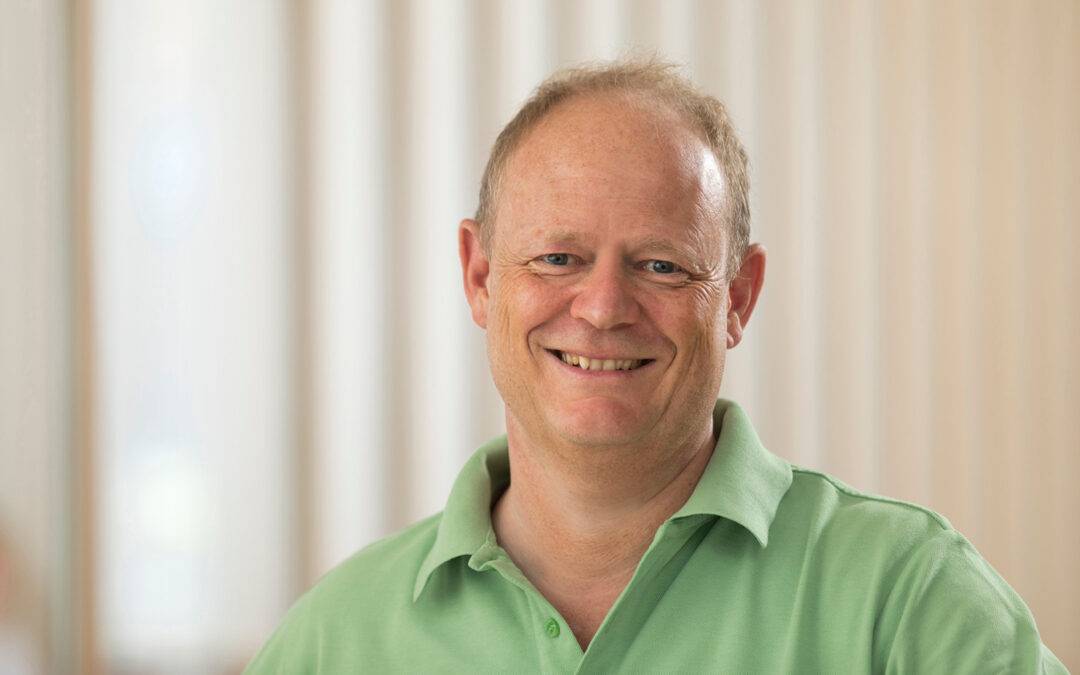 Smiling man in a light green polo shirt, indoors, looking at the camera.