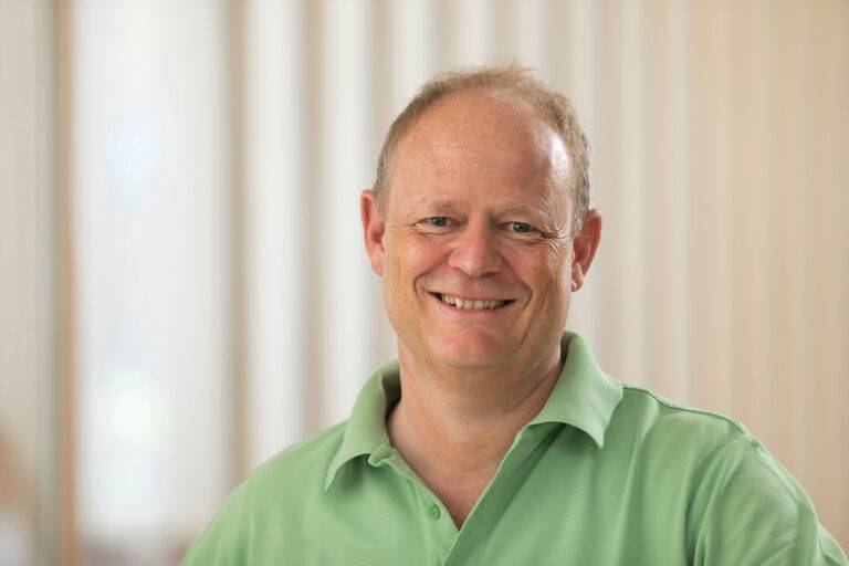 Smiling man in a light green polo shirt, indoors, looking at the camera.