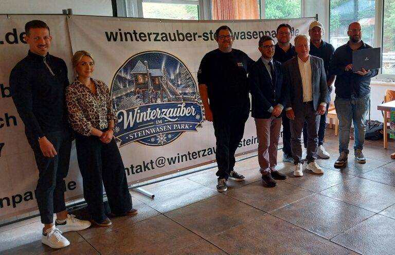 Group of people posing indoors in front of a banner reading 'Winterzauber im Steinwasen Park'.