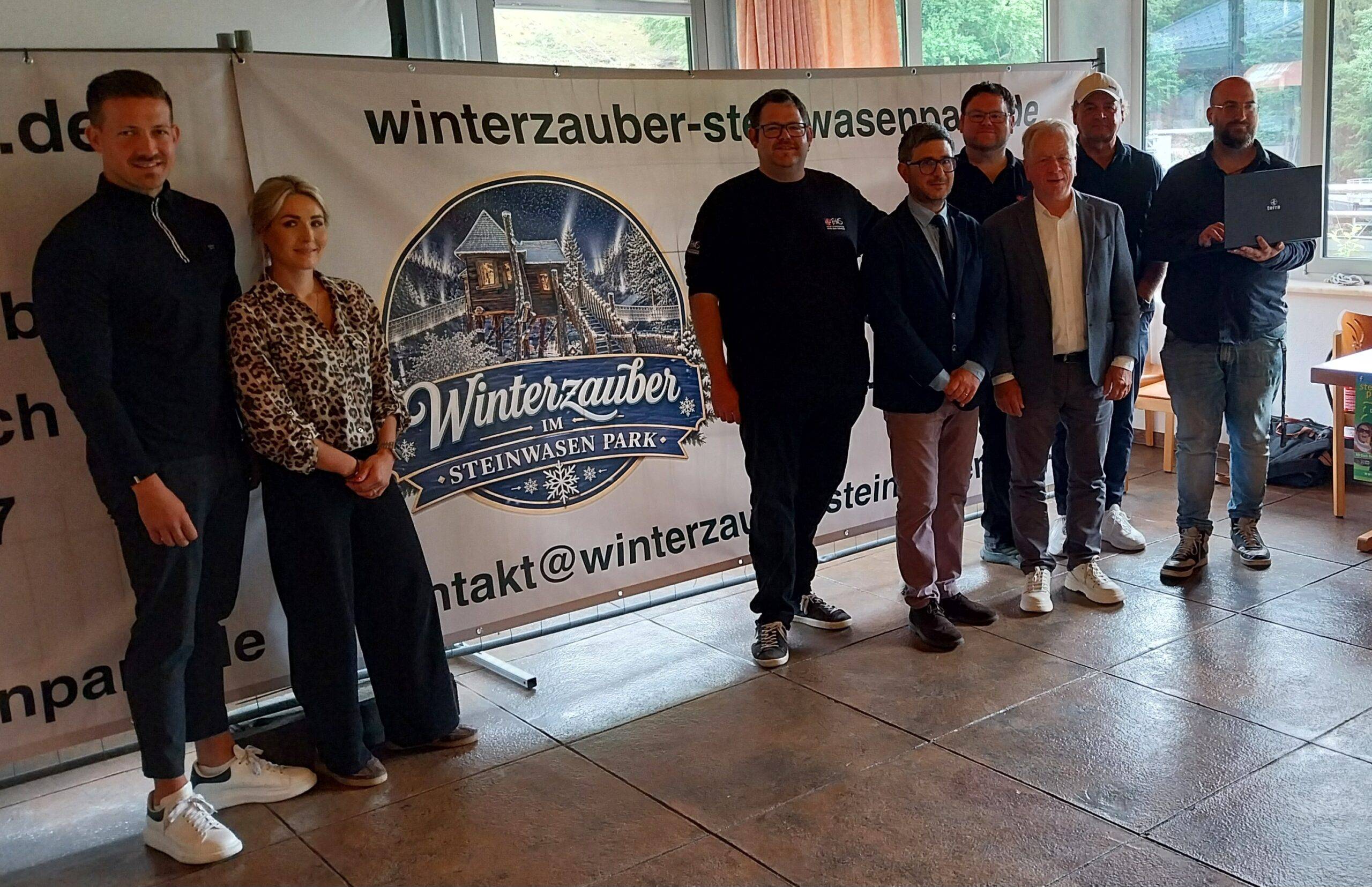 Group of people posing indoors in front of a banner reading 'Winterzauber im Steinwasen Park'.