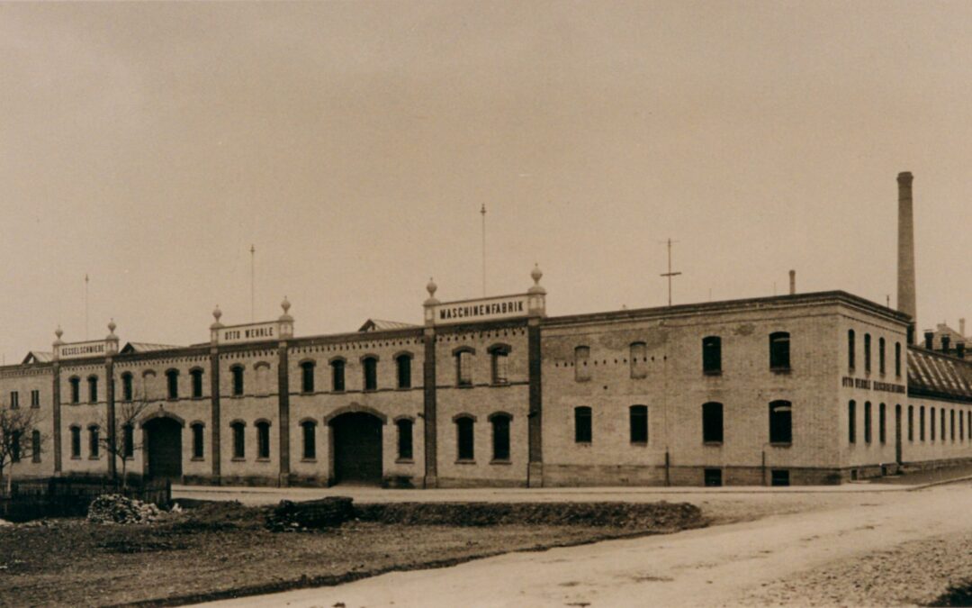 Historic brick factory building with arched windows and a tall chimney; sign reads MASCHINENFABRIK on the roofline.
