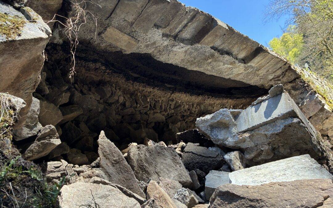 Rugged pile of broken rocks forming a cave-like opening, with blue sky and sparse vegetation beyond the entrance.