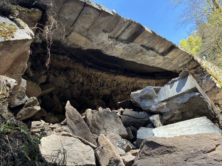 Rugged pile of broken rocks forming a cave-like opening, with blue sky and sparse vegetation beyond the entrance.