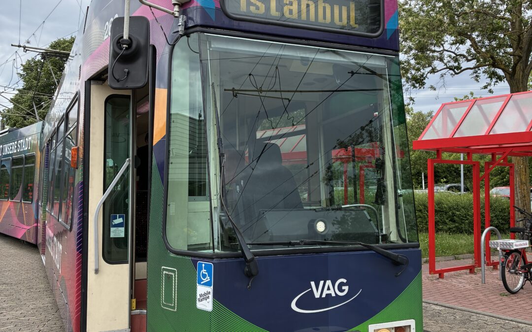 Front of a colorful tram with destination display reading ISTANBUL and route number 18, on tracks by a red shelter and trees in the background.