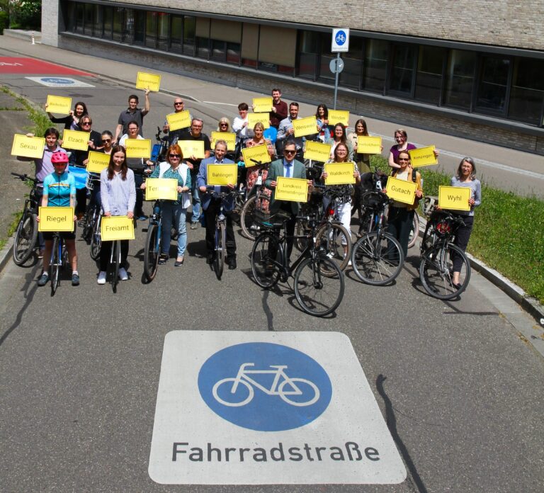 Group of cyclists holding yellow placards on a city street next to a modern brick building (Fahrradstraße).