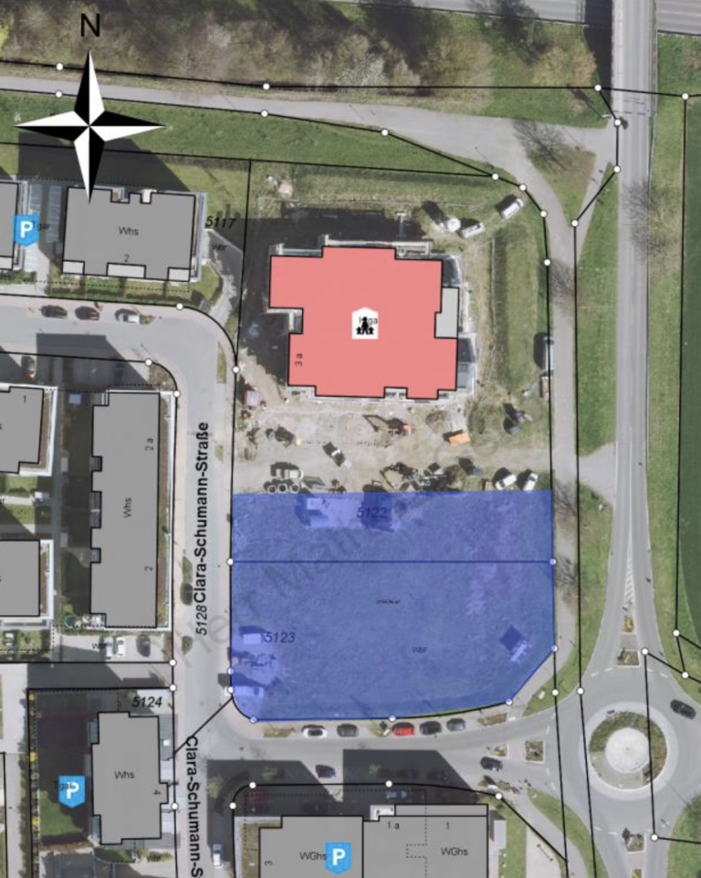 Aerial site map showing a red building, a large blue parcel to the south, and surrounding streets and compass rose at top left