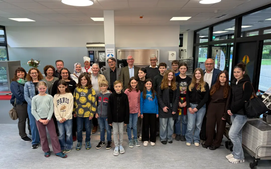 Group photo of students and adults in a modern kitchen or cafeteria with stainless steel appliances, posing for a group portrait.