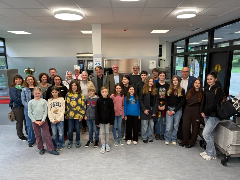 Group photo of students and adults in a modern kitchen or cafeteria with stainless steel appliances, posing for a group portrait.