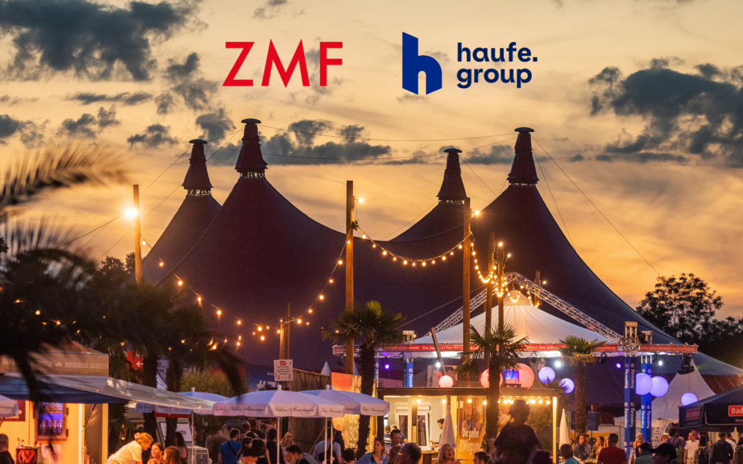 Festival scene at sunset with large tents and string lights; prominent ZMF and haufe group logos in the sky above the crowd.