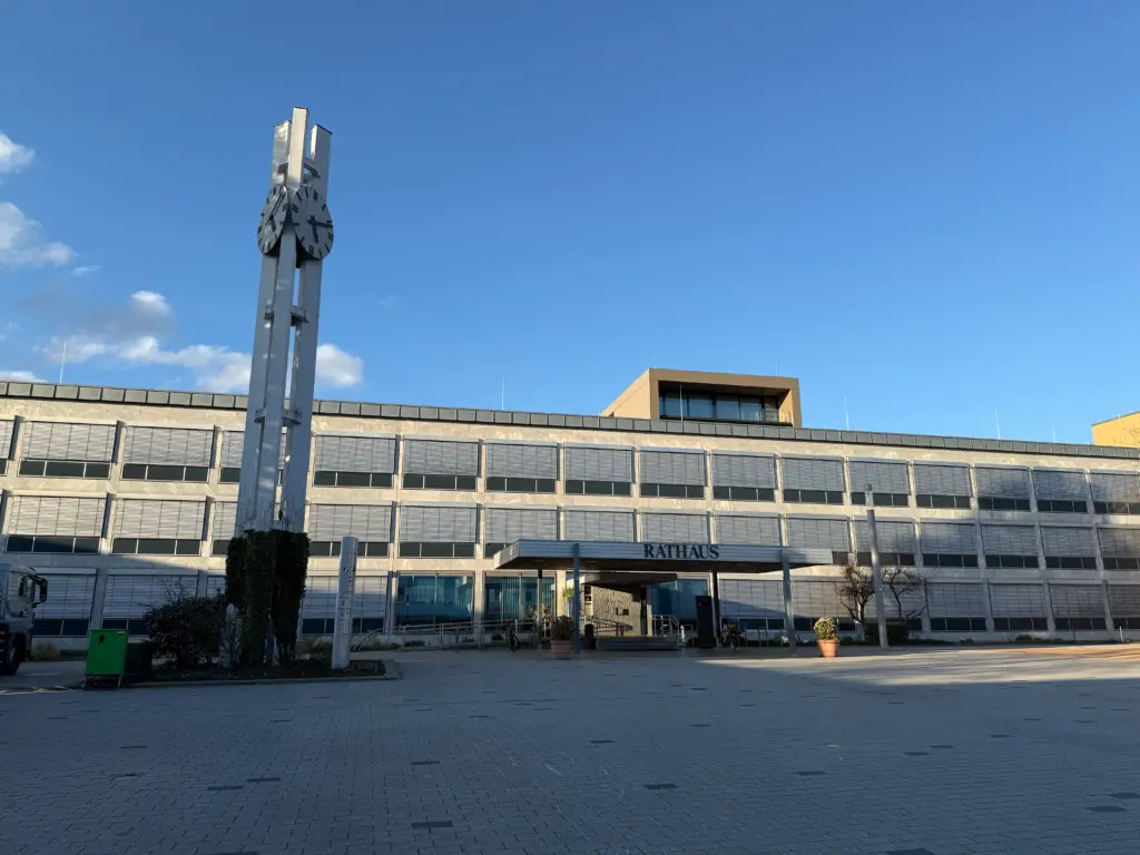 Municipal town hall with a tall metal clock tower showing two large clocks, set against a clear blue sky.