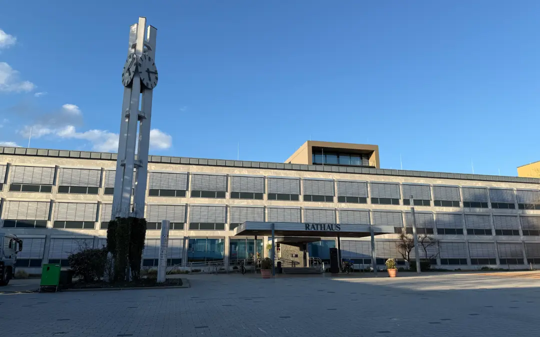 Municipal town hall with a tall metal clock tower showing two large clocks, set against a clear blue sky.