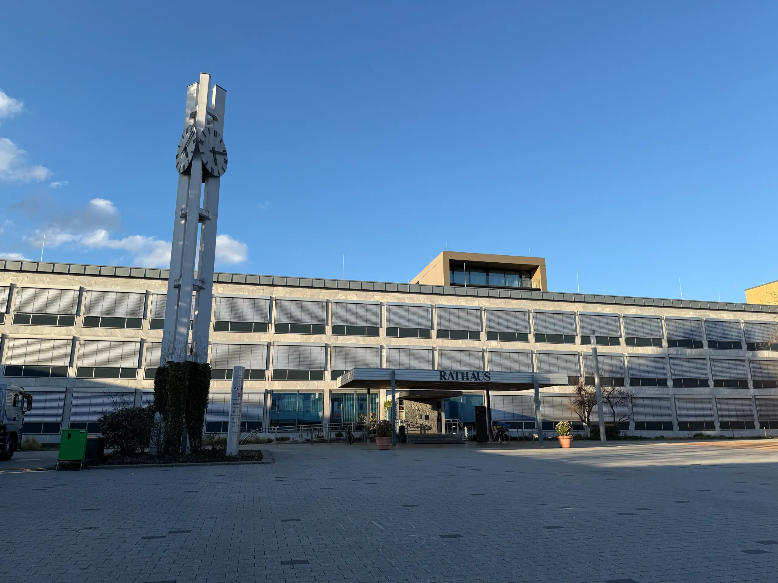 Municipal town hall with a tall metal clock tower showing two large clocks, set against a clear blue sky.