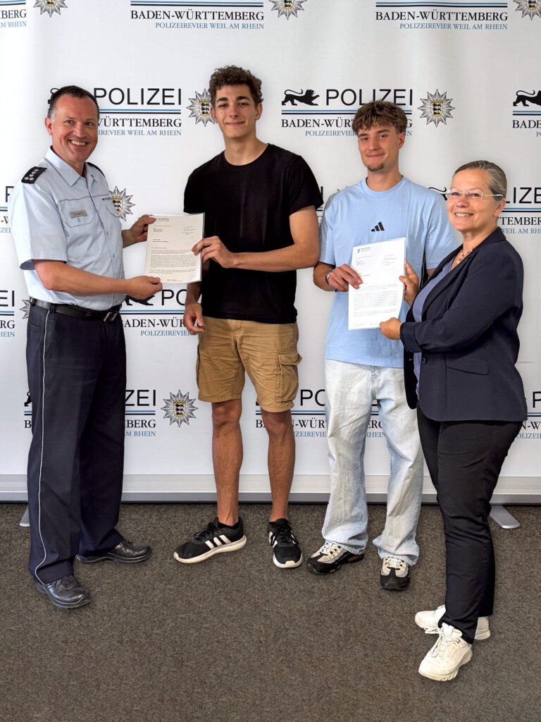 Police officer presents a certificate to a young man, flanked by two youths and a smiling woman, in front of a Baden-Württemberg Police backdrop.