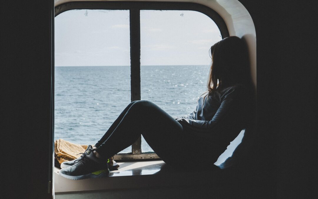 Person sitting in a boat’s window opening, gazing at the ocean outside.