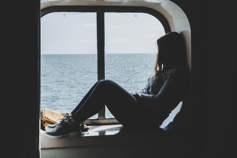 Person sitting in a boat’s window opening, gazing at the ocean outside.