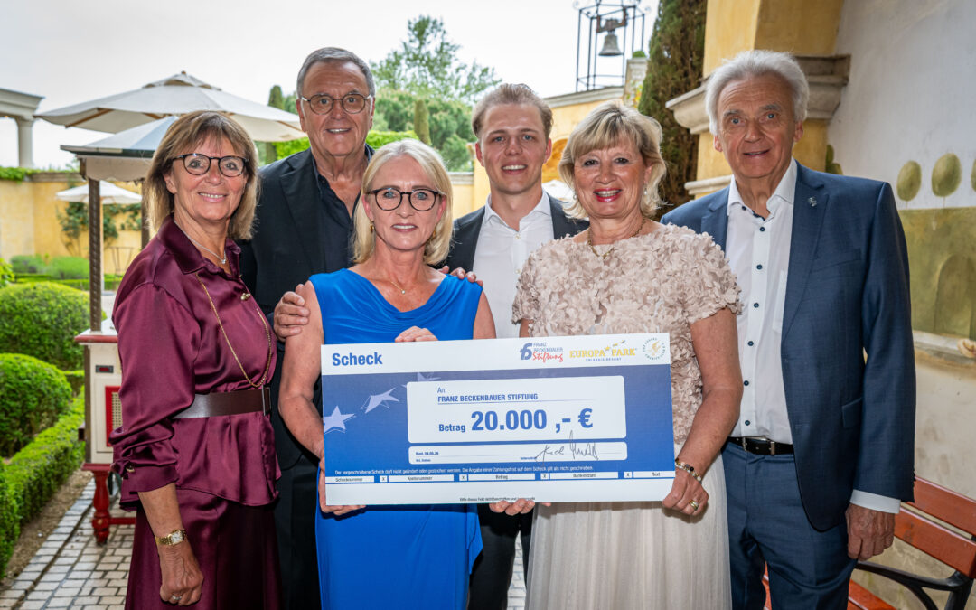 Five smiling adults stand outdoors, presenting a large ceremonial check for €20,000.