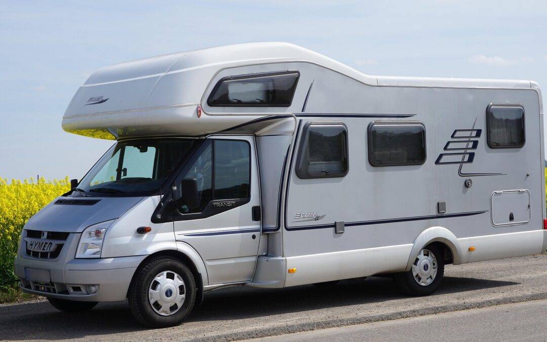 White motorhome parked on a country road beside a yellow flowering field under a blue sky.