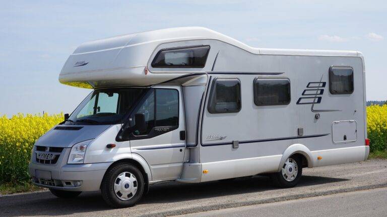 White motorhome parked on a country road beside a yellow flowering field under a blue sky.