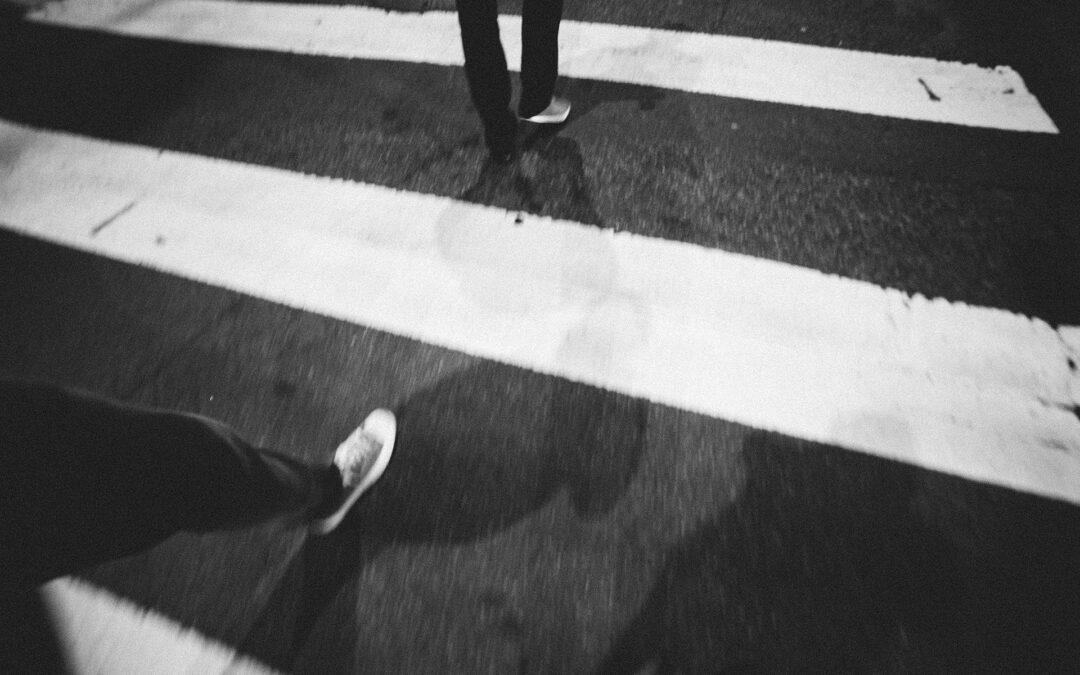 Person crossing a zebra-striped crosswalk at night, seen from above.