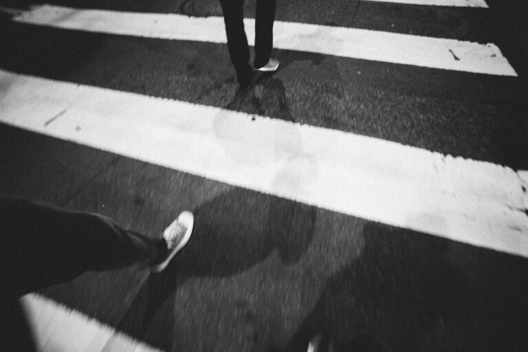 Person crossing a zebra-striped crosswalk at night, seen from above.