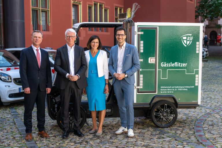 Four business professionals pose beside a green delivery trailer with the ASF logo in an outdoor urban setting, wearing suits and a blue dress center-left women smiling.