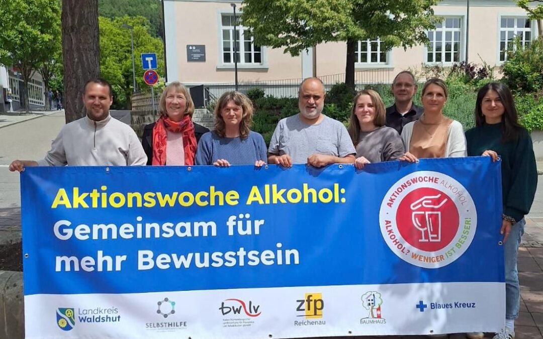 Group of eight people holding a large blue banner reading 'Aktionswoche Alkohol: Gemeinsam für mehr Bewusstsein' outdoors.