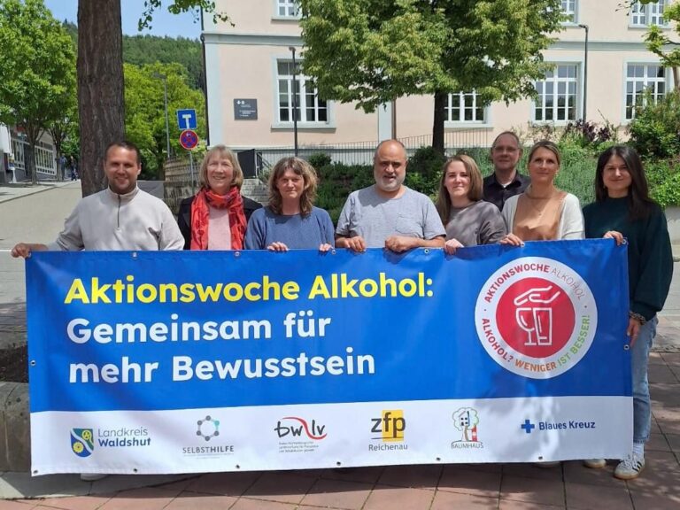 Group of eight people holding a large blue banner reading 'Aktionswoche Alkohol: Gemeinsam für mehr Bewusstsein' outdoors.