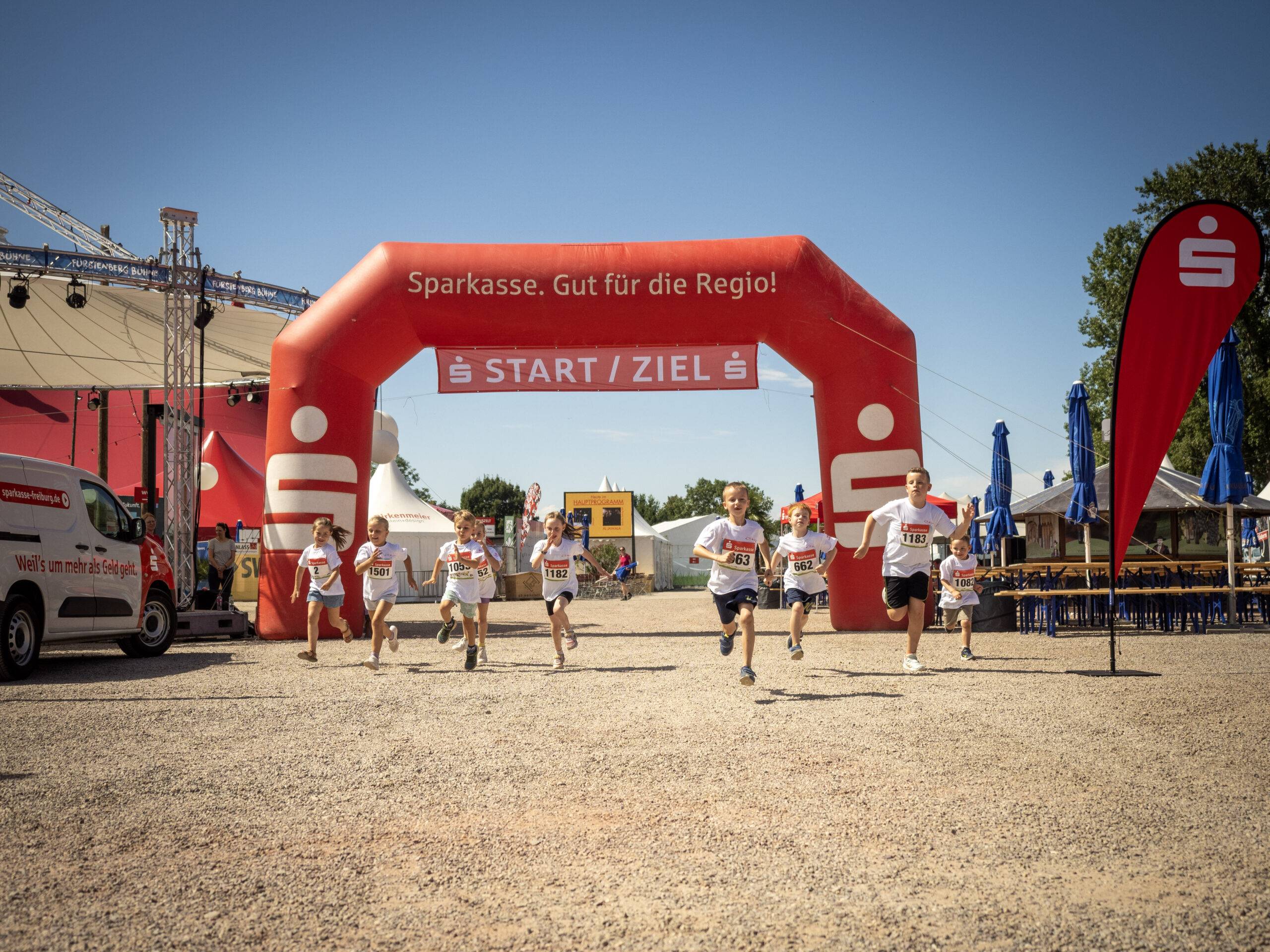 Young runners race under a red start arch labeled START/ZIEL at a daytime outdoor event.