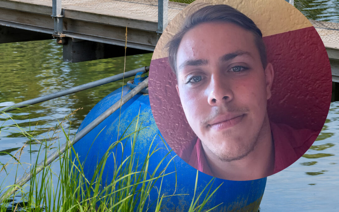 Close-up portrait of a young man overlaid on a blue buoy beside a lake and a wooden bridge.