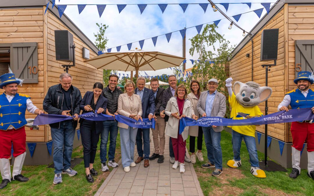 Group of people cutting a blue ribbon at a Europa Park Resort opening, flanked by two costumed mascots and EU bunting.