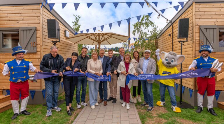 Group of people cutting a blue ribbon at a Europa Park Resort opening, flanked by two costumed mascots and EU bunting.