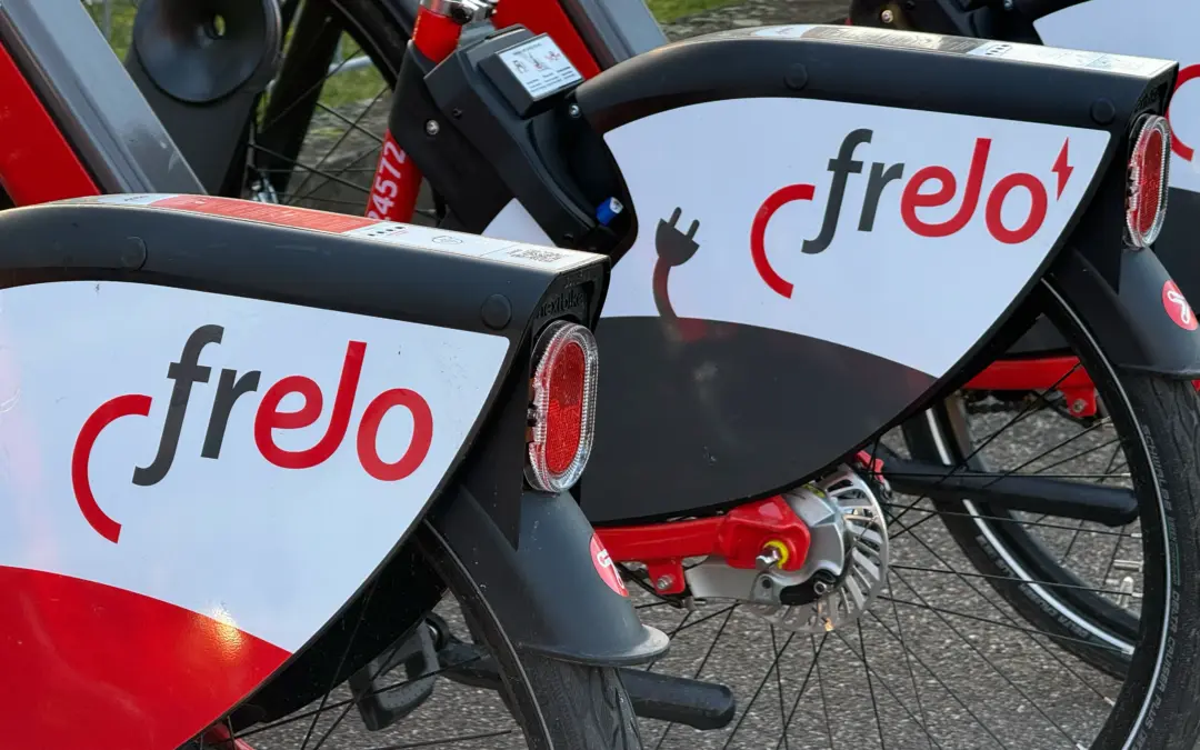 Close-up of stacked Frelo rental bikes with red frames, white branded panels, and visible rear lights and wheels.