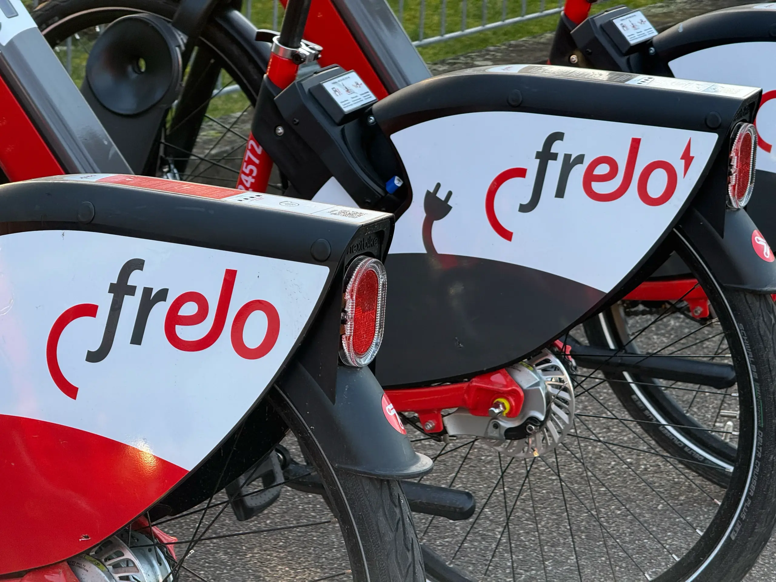 Close-up of stacked Frelo rental bikes with red frames, white branded panels, and visible rear lights and wheels.