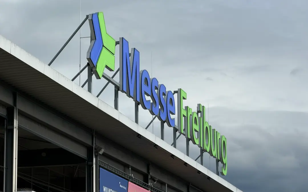 Exterior of a convention center with a large blue and green 'Messe Frankfurt' sign against a cloudy sky surface above the entrance.