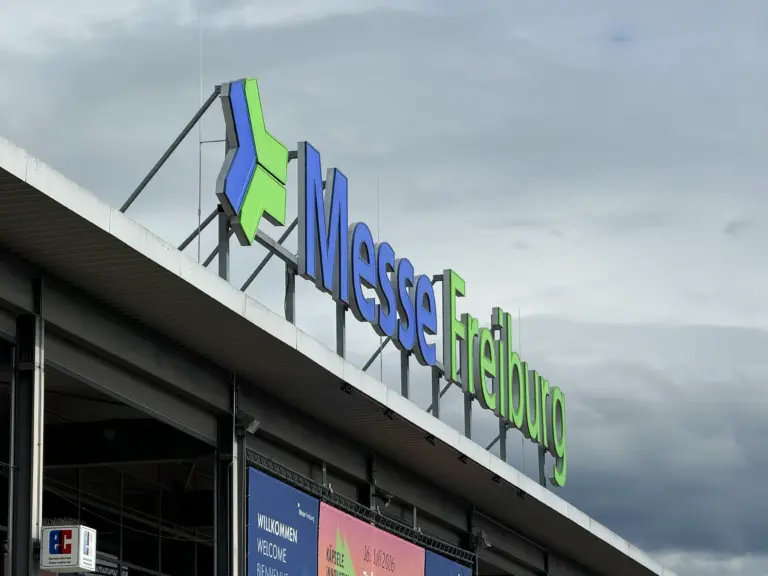 Exterior of a convention center with a large blue and green 'Messe Frankfurt' sign against a cloudy sky surface above the entrance.