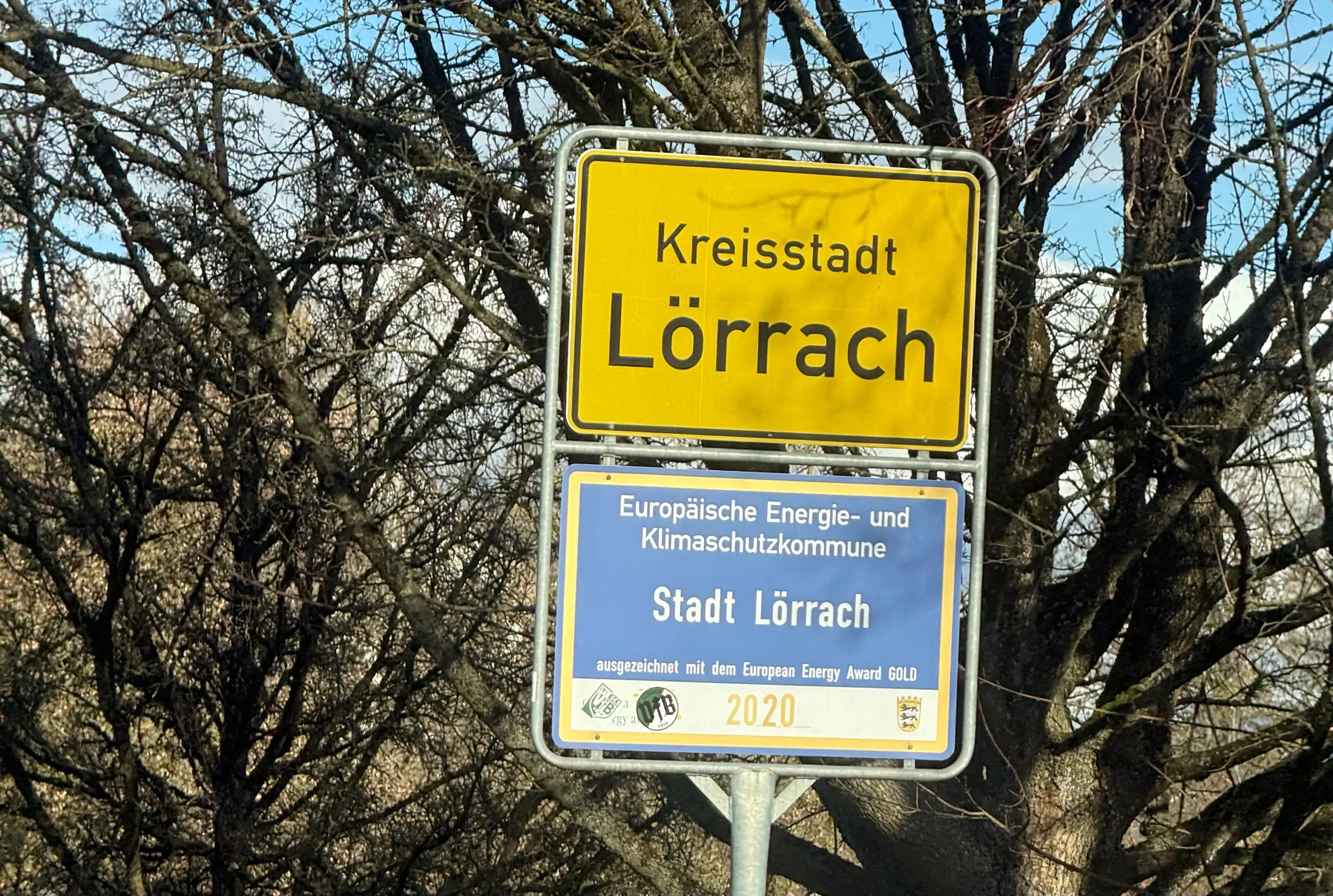 Yellow town sign reading 'Kreisstadt Lörrach' with a blue plaque below about European energy and climate protection municipality sign (city of Lörrach)