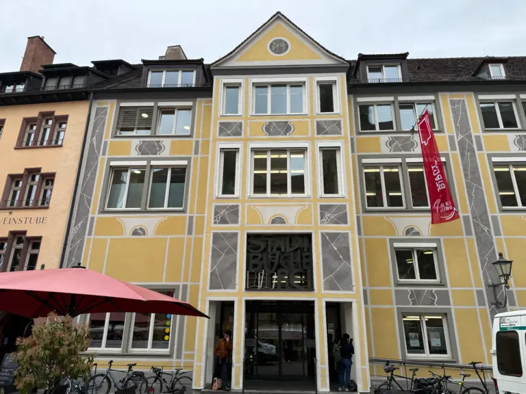 Colorful decorative building facade with yellow and gray geometric panels, many windows, and a red flag outside.