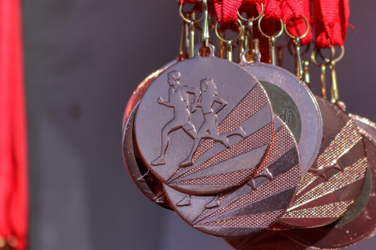 Close-up of bronze running medals hanging from red ribbons, showing two runners mid-stride against geometric patterns.