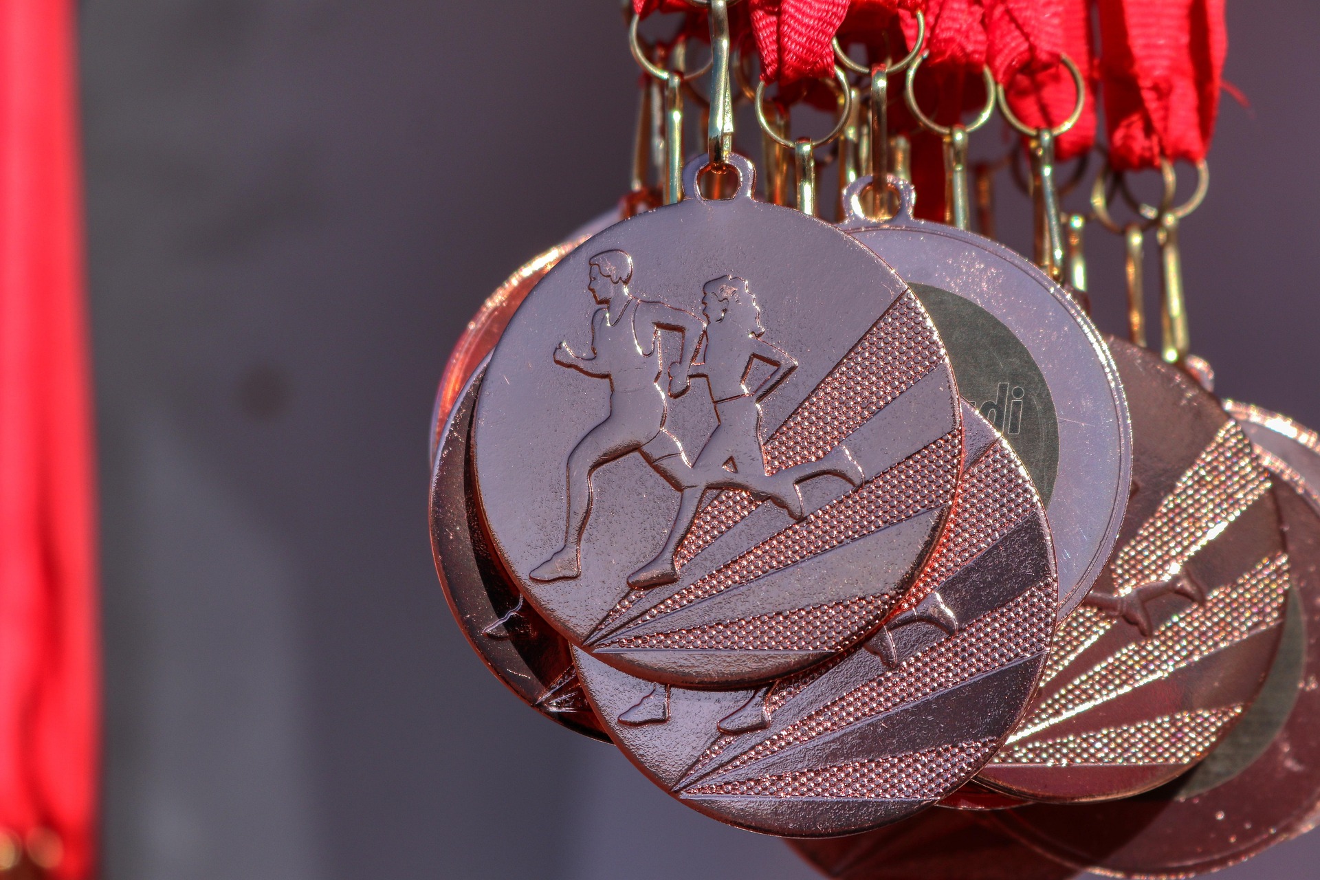 Close-up of bronze running medals hanging from red ribbons, showing two runners mid-stride against geometric patterns.