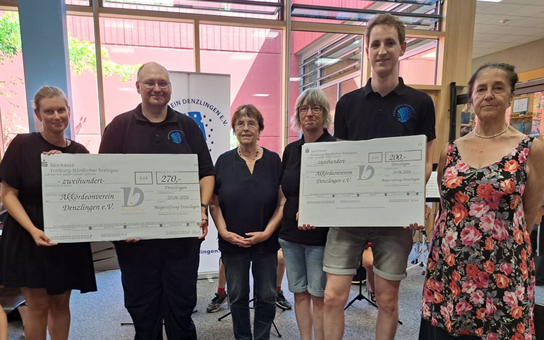Six people indoors, two holding oversized donation checks and smiling for the photo.