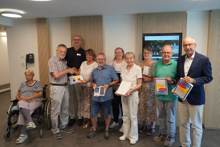 Group of eleven adults posing indoors for a photo; several hold iPhone boxes as prizes.