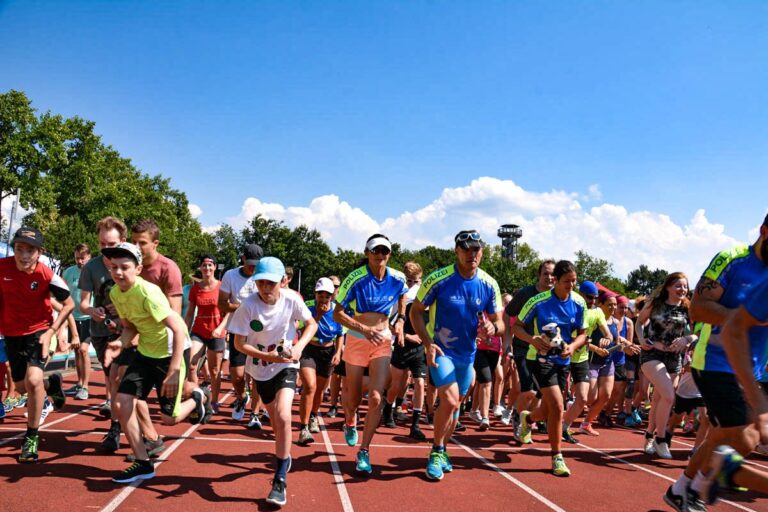 Group of runners at the starting line on an outdoor track under a blue sky, wearing colorful athletic gear.